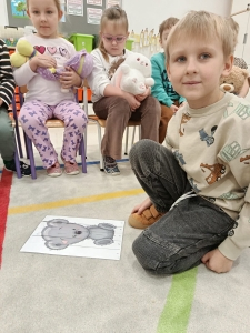 Dzieci siedzą w szkolnej sali, jedno dziecko na podłodze