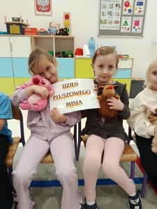 Dwie dziewczynki trzymają tabliczkę z napisem "Dzień Pluszowego Misia"