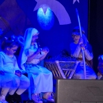 Dzieci w strojach przedstawiają scenę z jasełkami na tle niebieskiego oświetlenia