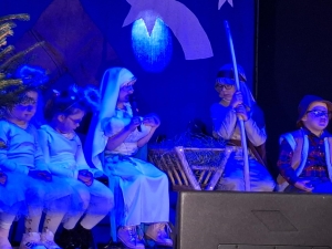 Dzieci w strojach przedstawiają scenę z jasełkami na tle niebieskiego oświetlenia