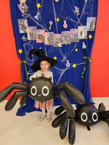 Dziewczynka w czarnym kapeluszu trzyma balon w kształcie pająka