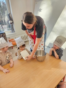 Kobieta z dziećmi w czapkach kuchennych przy stole