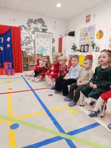 Dzieci siedzą w szkolnym pomieszczeniu na krzesłach