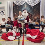 Dzieci otrzymują prezenty od Mikołaja w szkolnej sali