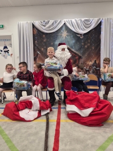 Dzieci otrzymują prezenty od Mikołaja w szkolnej sali