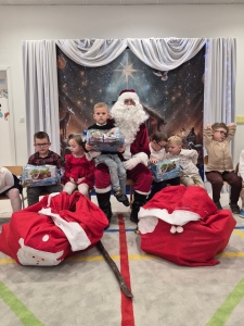 Dzieci siedzą z Mikołajem, trzymając prezenty. Na podłodze leżą worki