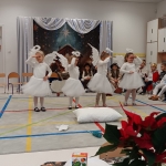 Dzieci w strojach aniołów tańczą na scenie w szkole. W tle widoczny jest dekoracyjny tłum