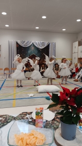 Dzieci w strojach aniołów tańczą na scenie w szkole. W tle widoczny jest dekoracyjny tłum