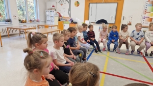 Grupa dzieci siedzi w kole na podłodze w przedszkolu