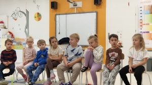 Grupa dzieci siedzi na krzesłach w pomieszczeniu szkolnym