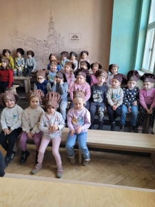 Grupa dzieci w czapkach siedzi na ławkach w pomieszczeniu
