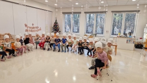 Grupa dzieci w czapkach kuchennych siedzi w sali z choinką