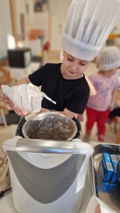 Dziecko w czapce kuchennej wsypuje składniki do maszyny