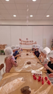 Dzieci w czepkach kuchennych robią ciasteczka na długim stole